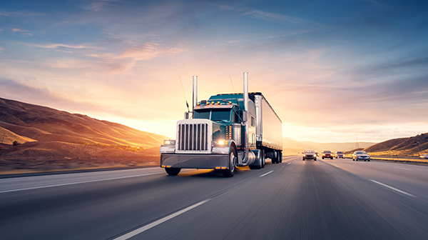 A truck hauling solar equipment on a highway at sunrise
